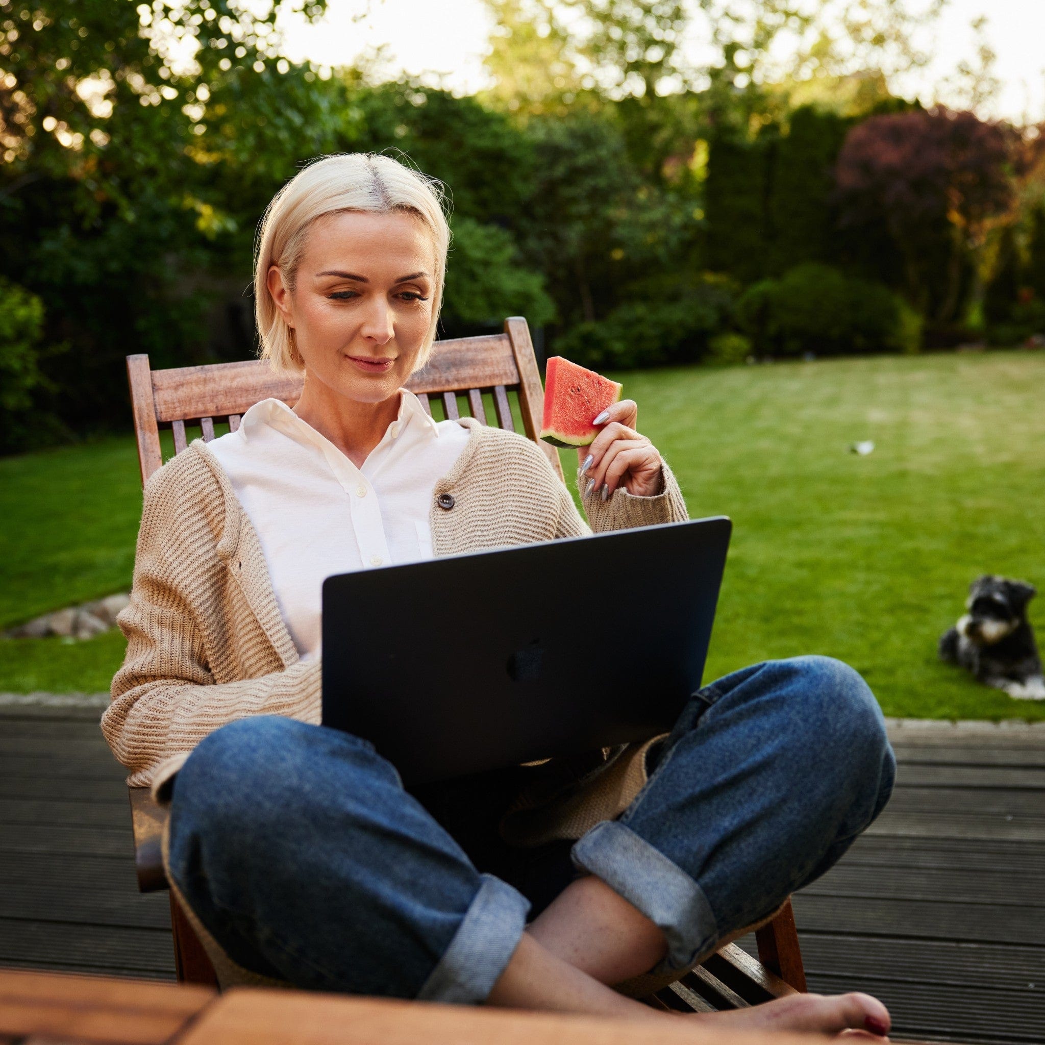 Frau sitzt draußen am Laptop auf einem Gartenstuhl mit Annabelle’s CozyPad – weiche Sitzauflage für komfortables Arbeiten im Freien