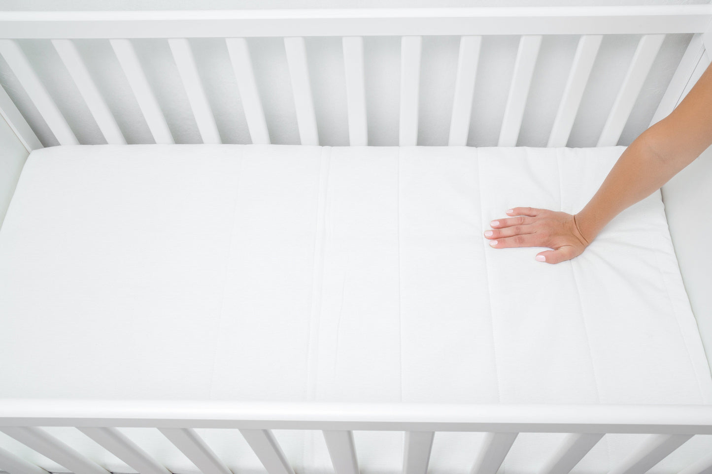 Hand liegt auf der BellaSleep Baby Matratze 10 cm im Babybett – ergonomische, atmungsaktive Matratze für sicheren Babyschlaf