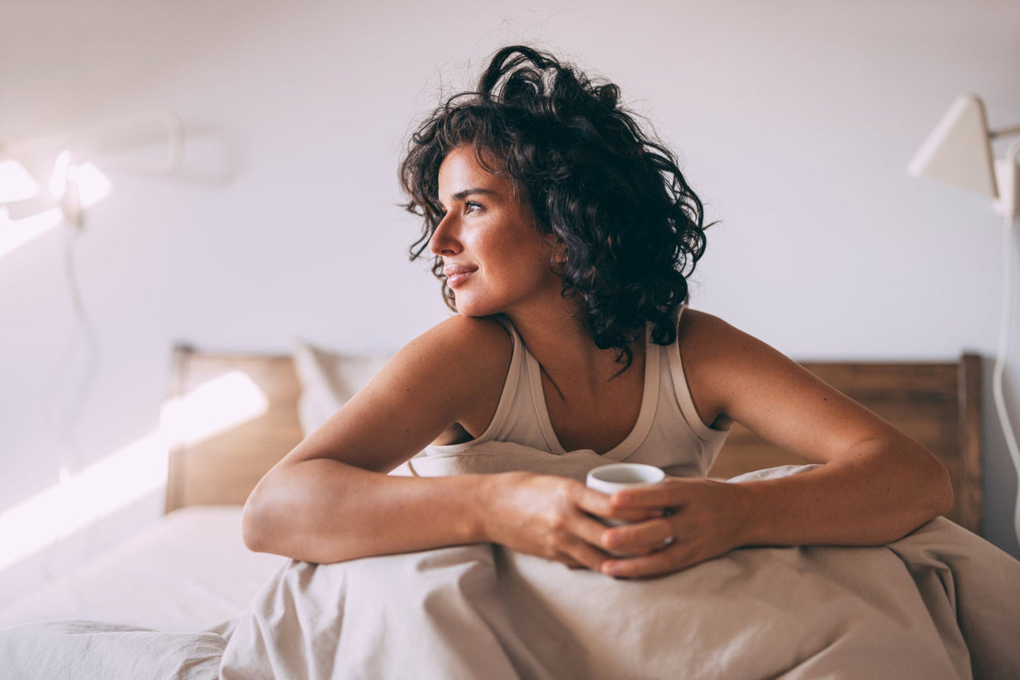 Frau sitzt entspannt im Bett auf der BellaSleep Deluxe Matratze 25 cm und trinkt genüsslich eine Tasse Kaffee am Morgen