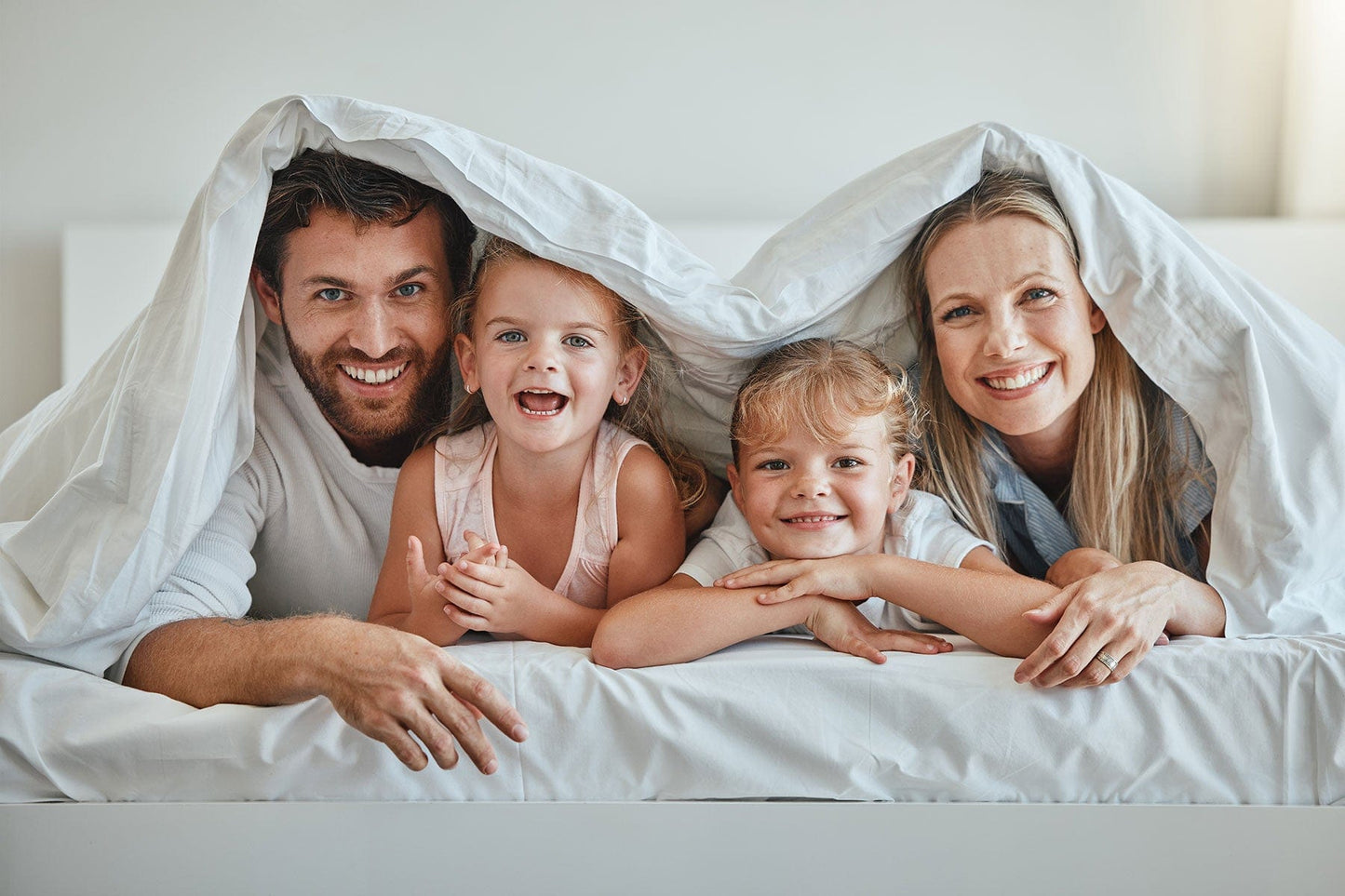 Glückliche Familie liegt gemeinsam unter der Bettdecke – Geborgenheit, Komfort und Wohlbefinden mit Annabelle’s Schlafprodukten