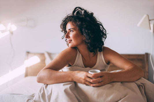 Frau sitzt entspannt im Bett auf der BellaSleep Deluxe Matratze 25 cm und trinkt genüsslich eine Tasse Kaffee am Morgen