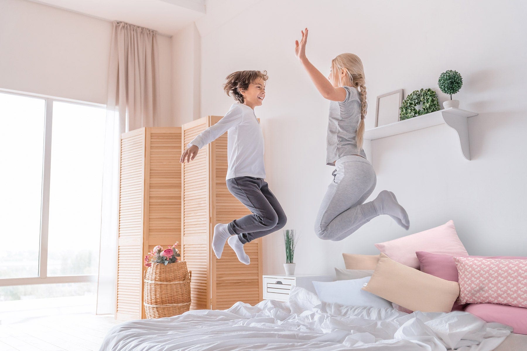 Kinder hüpfen fröhlich auf dem Bett mit Annabelle’s SleepGuard Kids – strapazierfähige, geräuscharme Inkontinenzauflage für Alltag und Spaß